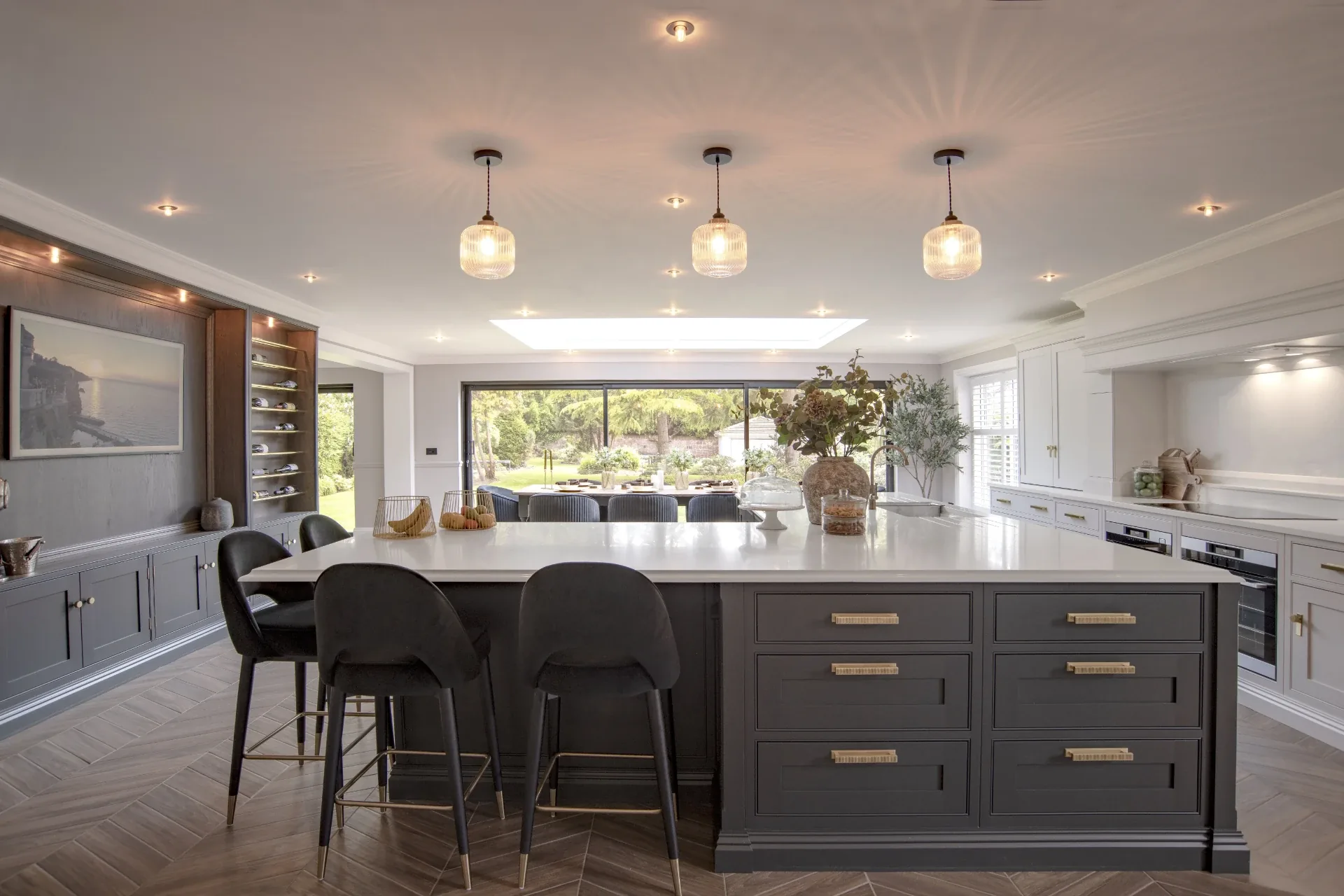 Dark grey island with white quartz worktop and brass handles in an open-plan kitchen